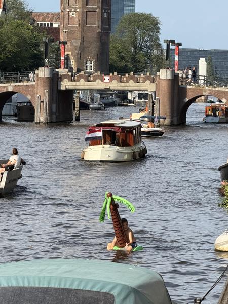 This vibrant photo captures a lively summer day on the canals of Oudeschans, Uilenburg, Amsterdam, with several boats navigating the water